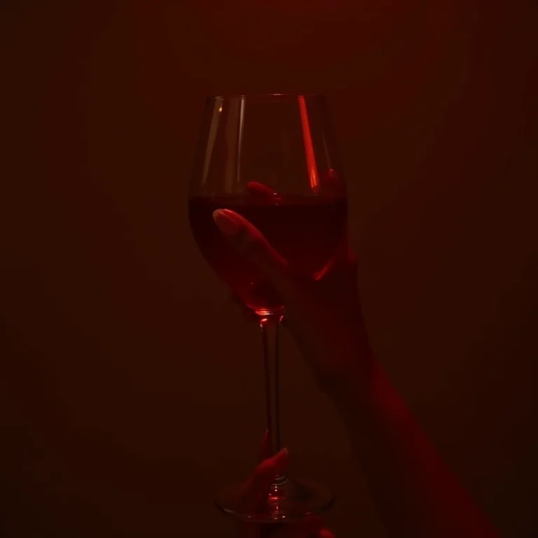 Mão de mulher com esmalte vermelho segurando taça de vinho tinto