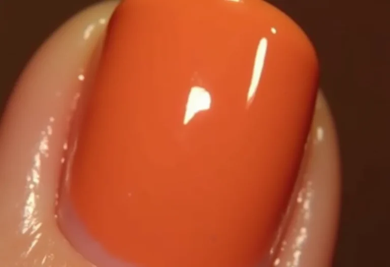 Mãos femininas segurando batom dourado com esmalte nude brilhante.