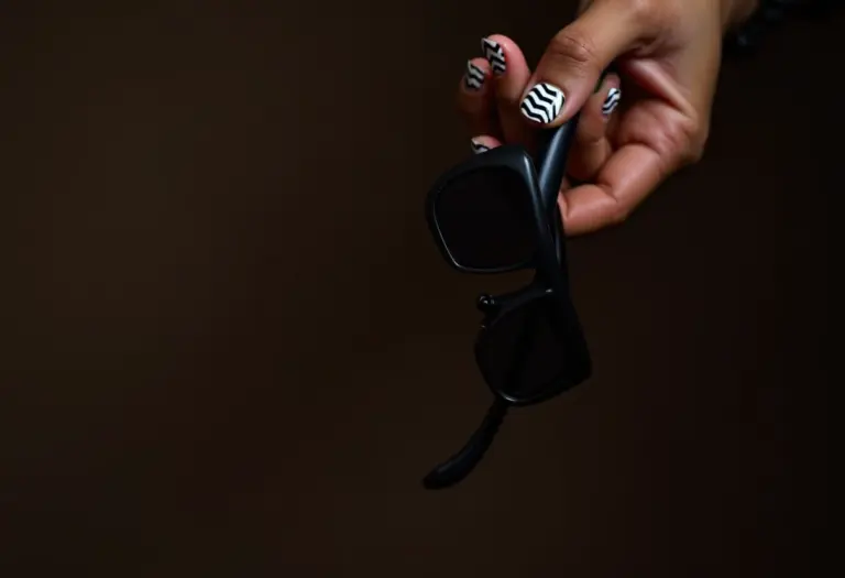 Unhas decoradas masculinas com design geométrico segurando óculos de sol pretos.